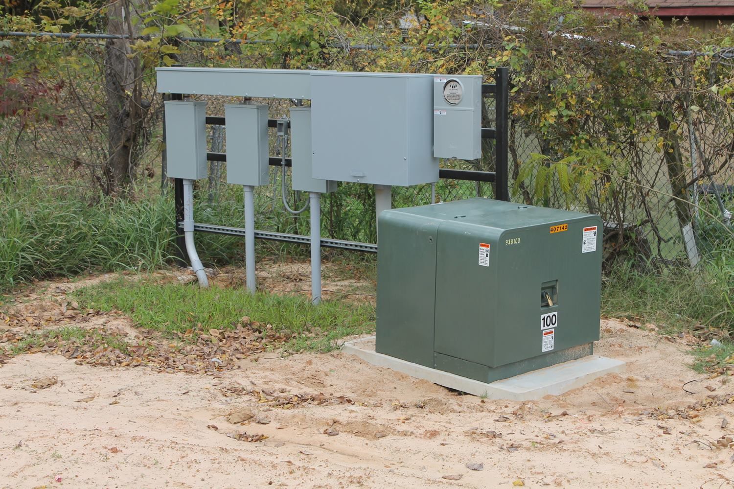 A green pad-mounted electrical transformer sits on a concrete pad next to gray utility meter enclosures on a metal rack.