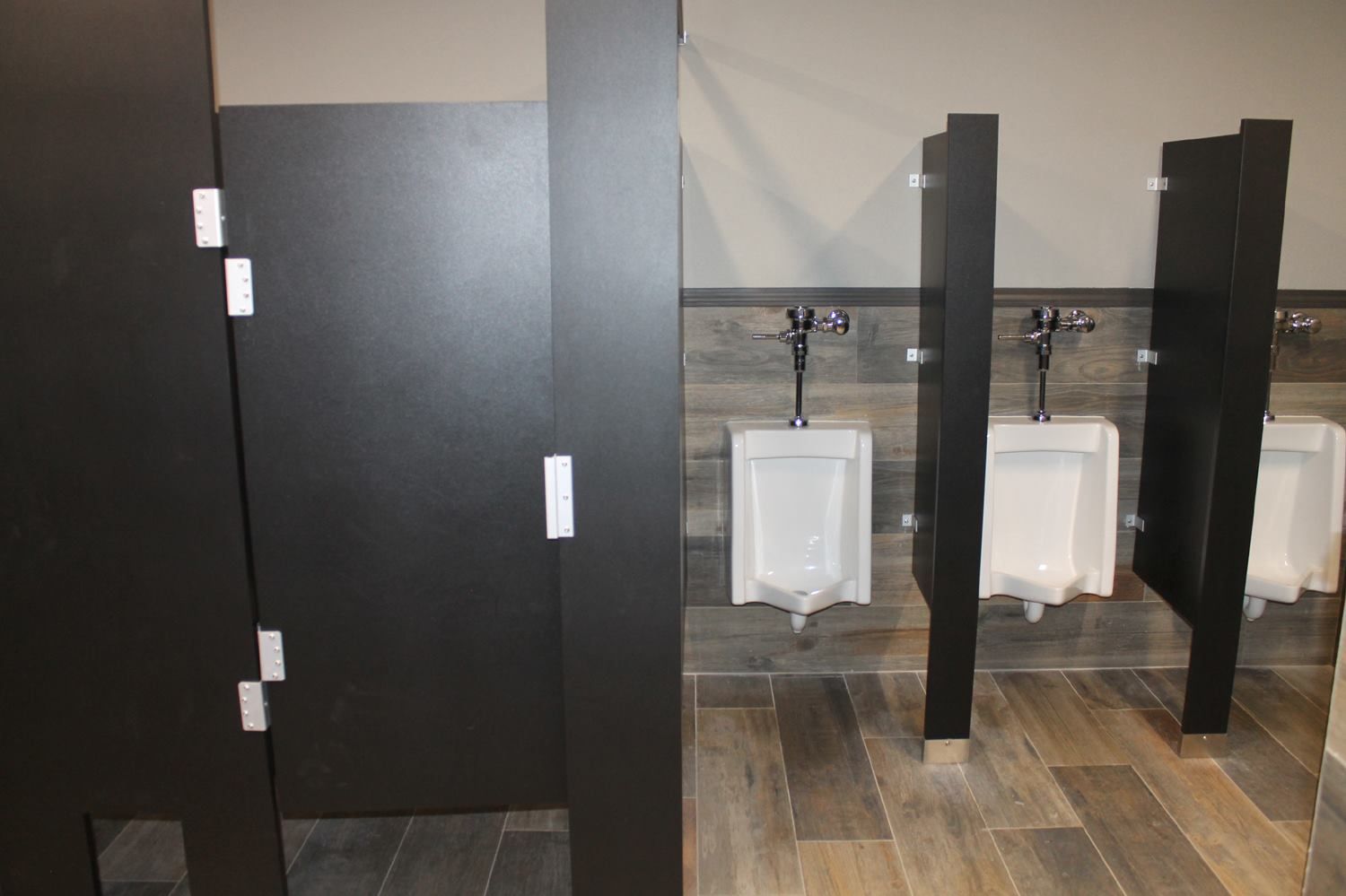 Modern restroom with a stall on the left and three wall-mounted white urinals separated by dark privacy dividers.