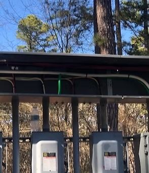 Outdoor electrical conduits and wiring mounted on a structure against a background of trees.