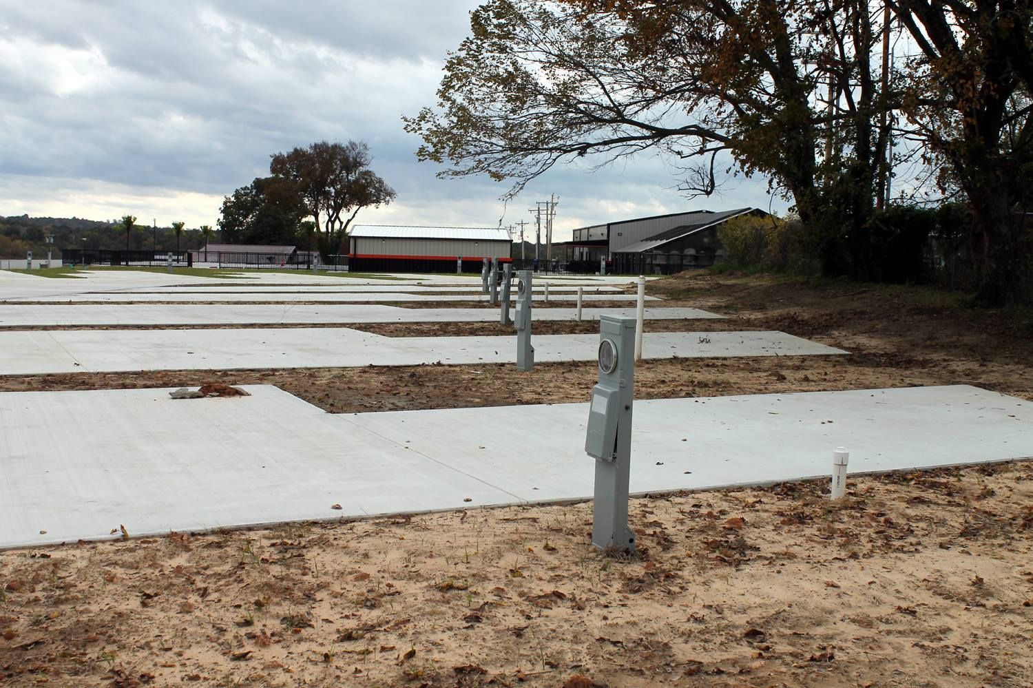 Concrete RV pads with utility hookups arranged in rows in an outdoor park setting under a cloudy sky.