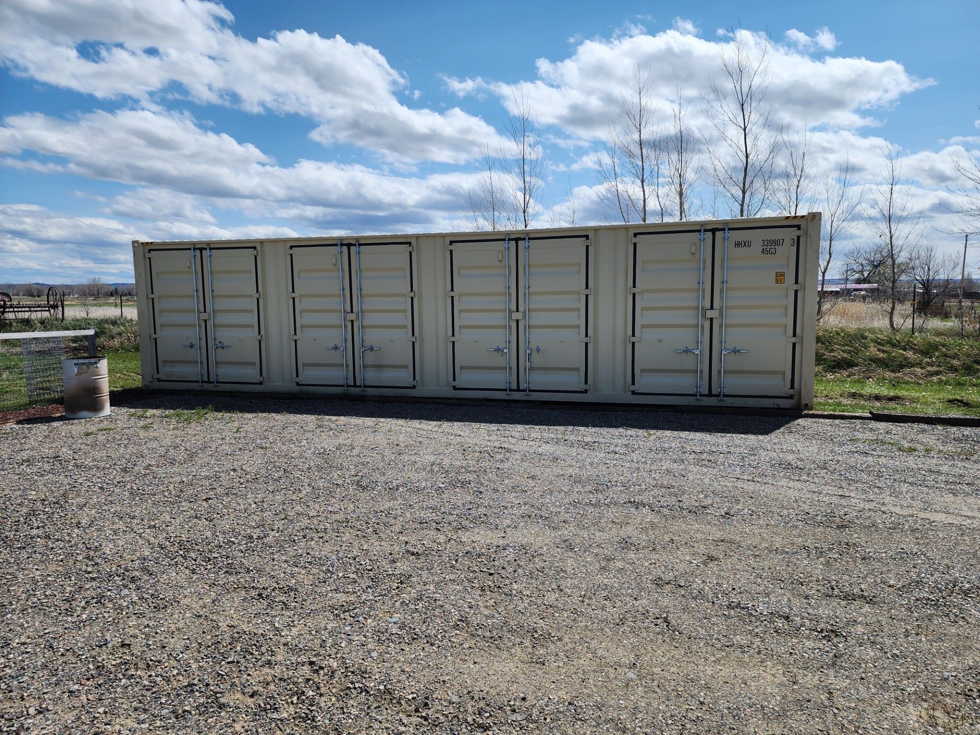 Storage containers with multiple doors on a gravel lot, under a blue sky.