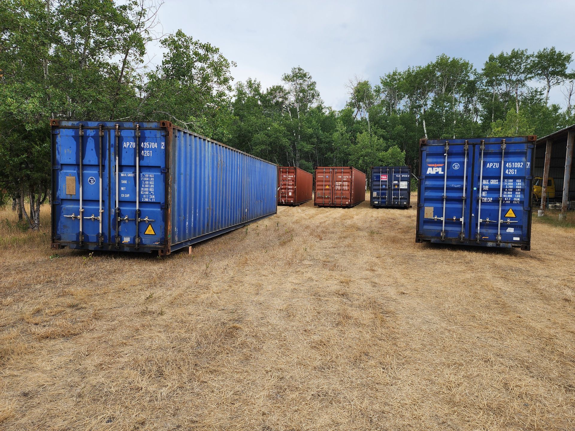 A row of shipping containers are lined up in a dirt field