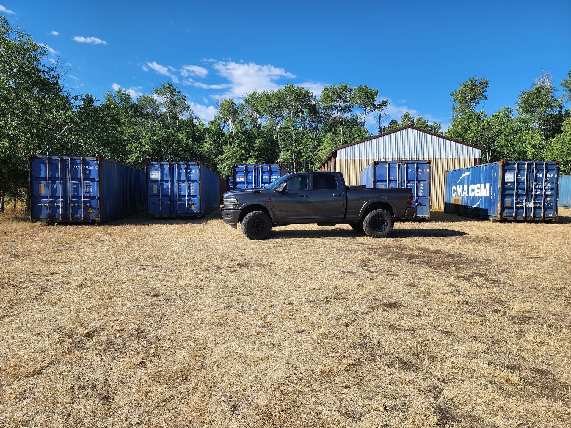 A truck is parked in a field next to a row of shipping containers.