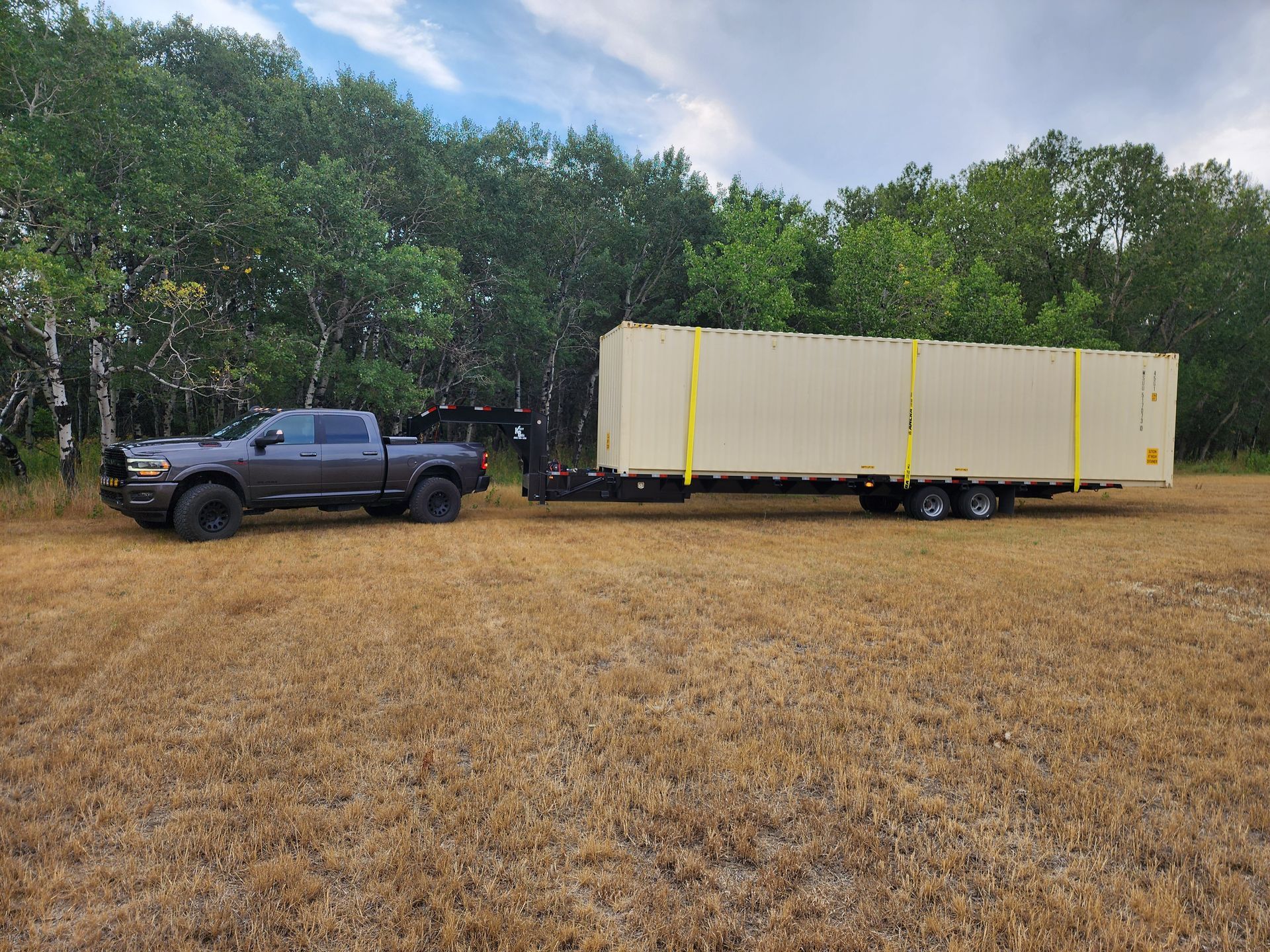 A truck is towing a trailer with a container on it in a field.