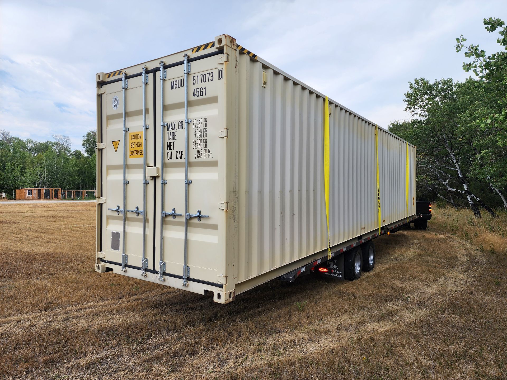 A shipping container is sitting on top of a trailer in a field.