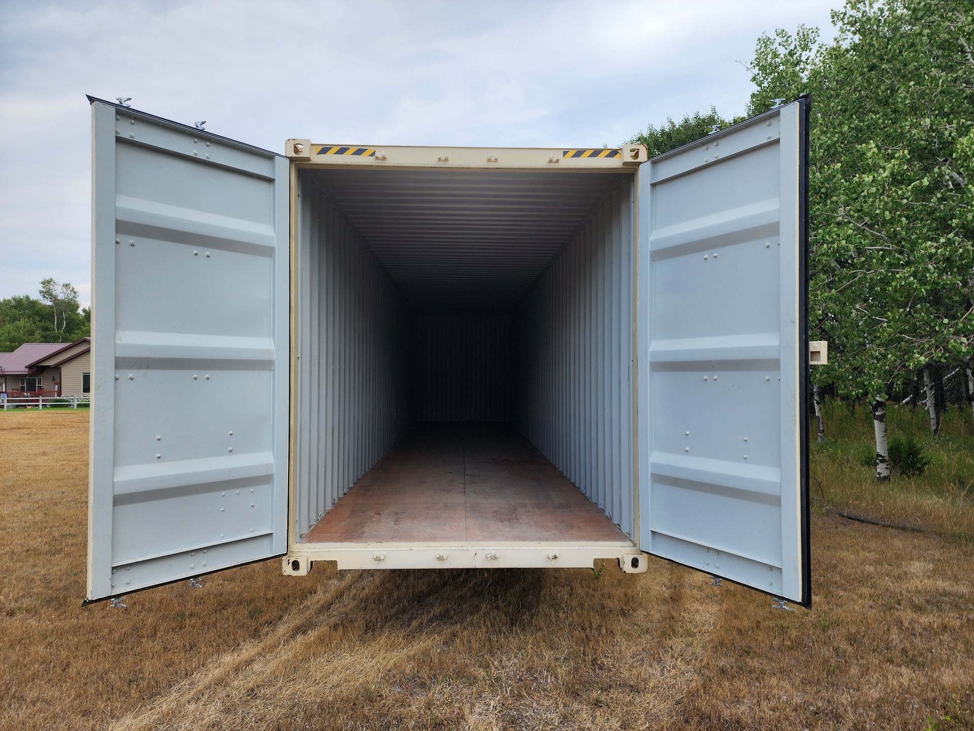An empty shipping container with its doors open in a field.