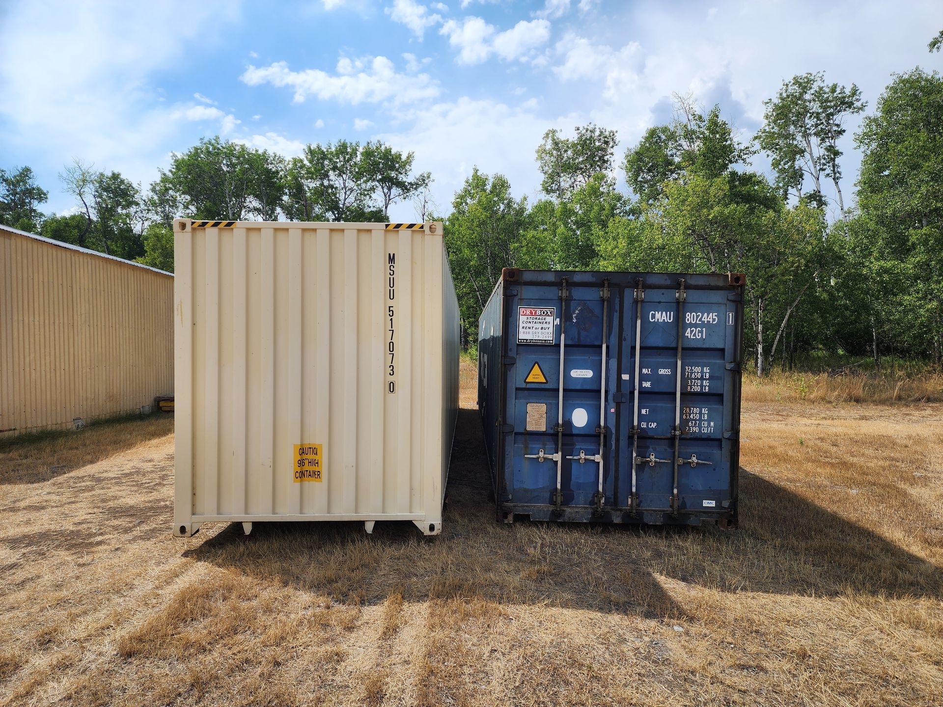 Two shipping containers are sitting next to each other in a field.