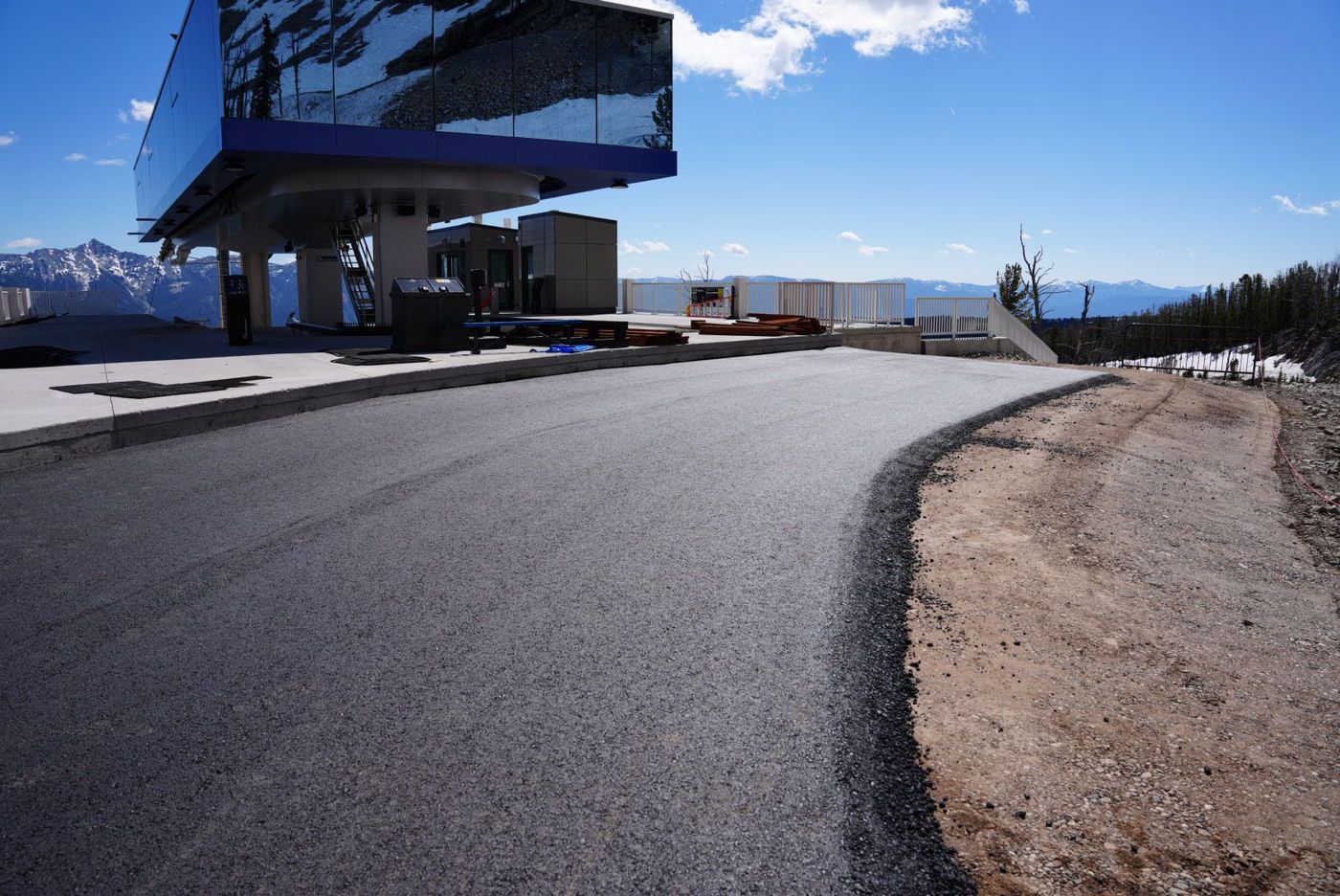 Curved paved road beside a modern glass building under a bright blue sky