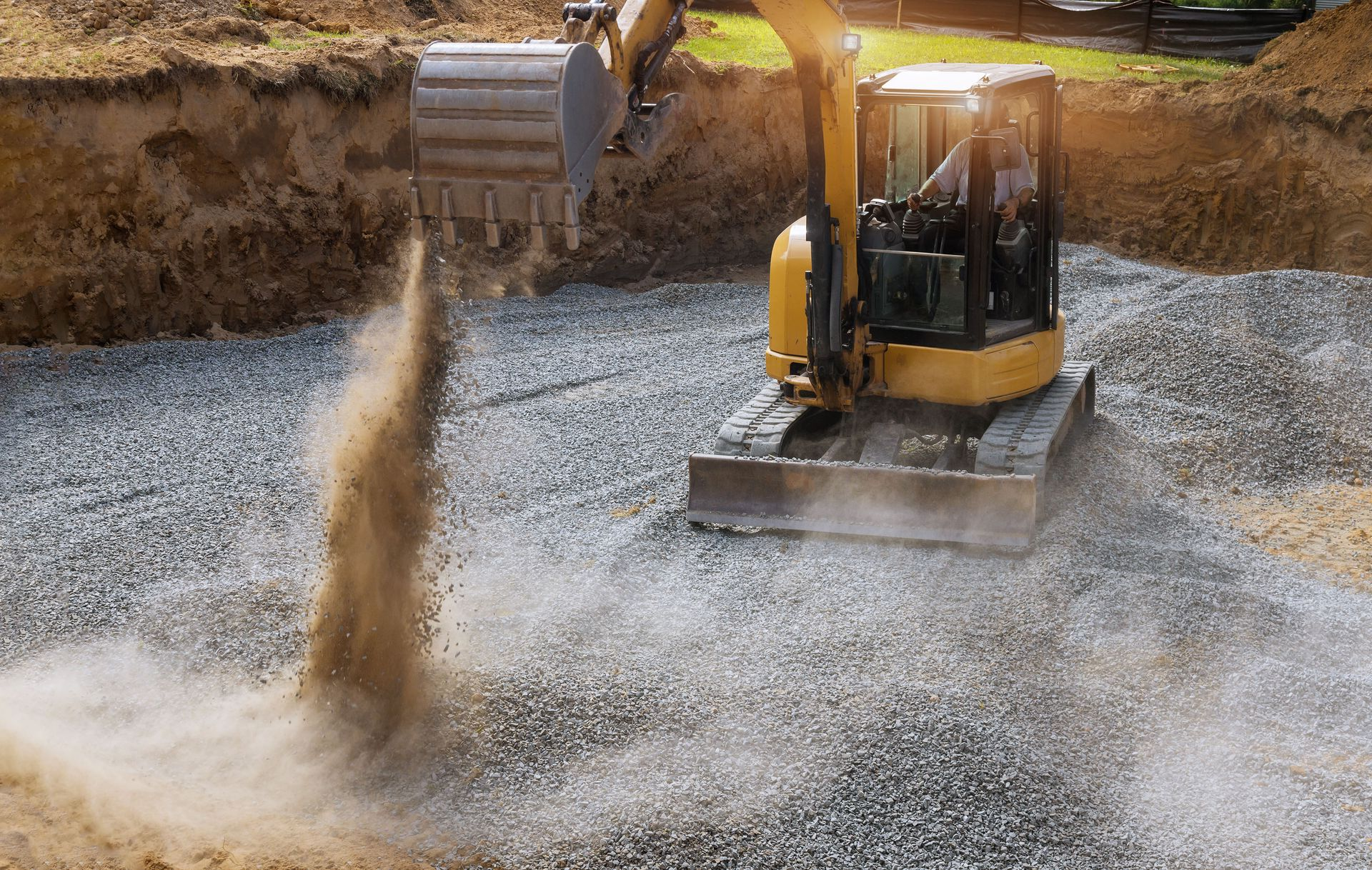Excavator digging gravel at a construction site, kicking up a plume of dust.