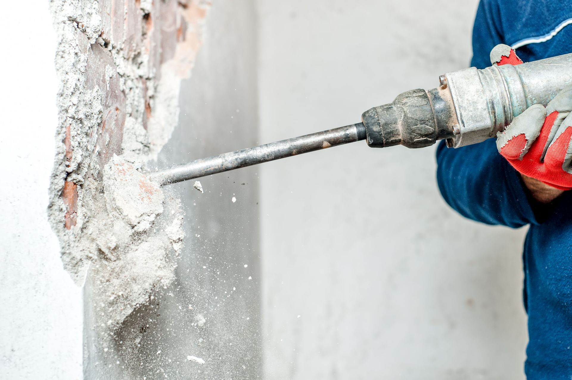 Worker using a jackhammer to break concrete from a wall during demolition