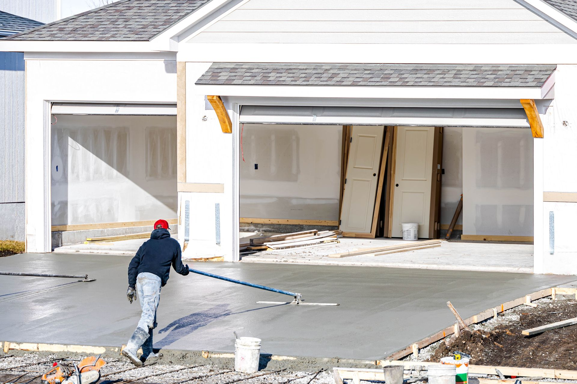 Worker spraying concrete driveway in front of a new house under construction