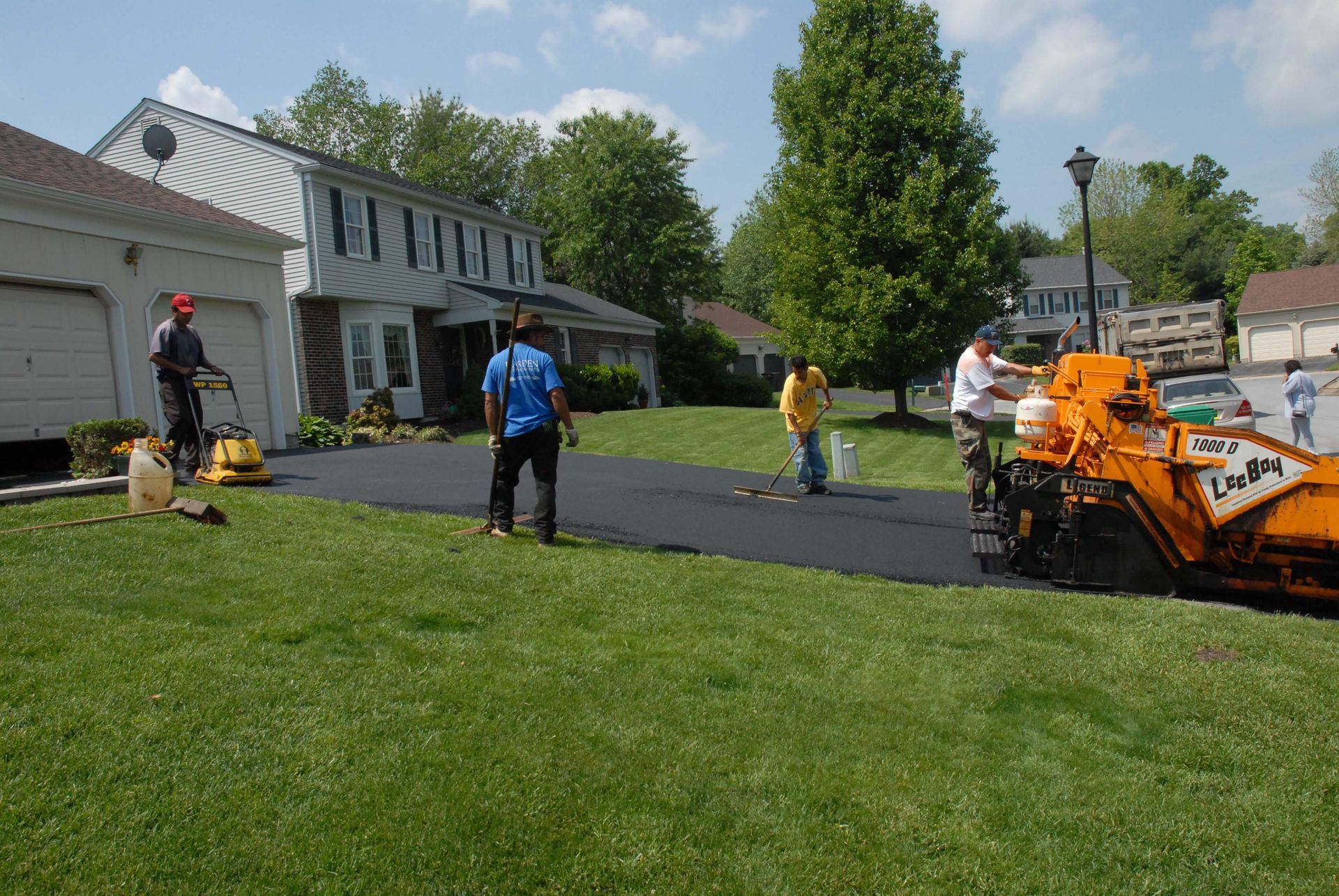 Road paving crew working outside a house with an orange paving machine and fresh black asphalt