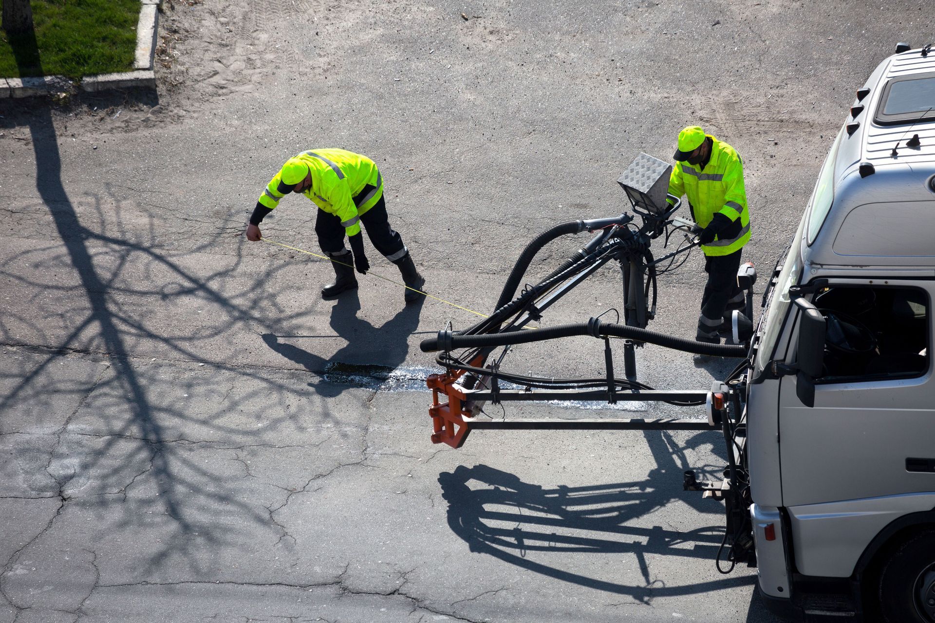 Two workers in neon safety gear inspect a white utility truck with a mounted crane on cracked pavement.