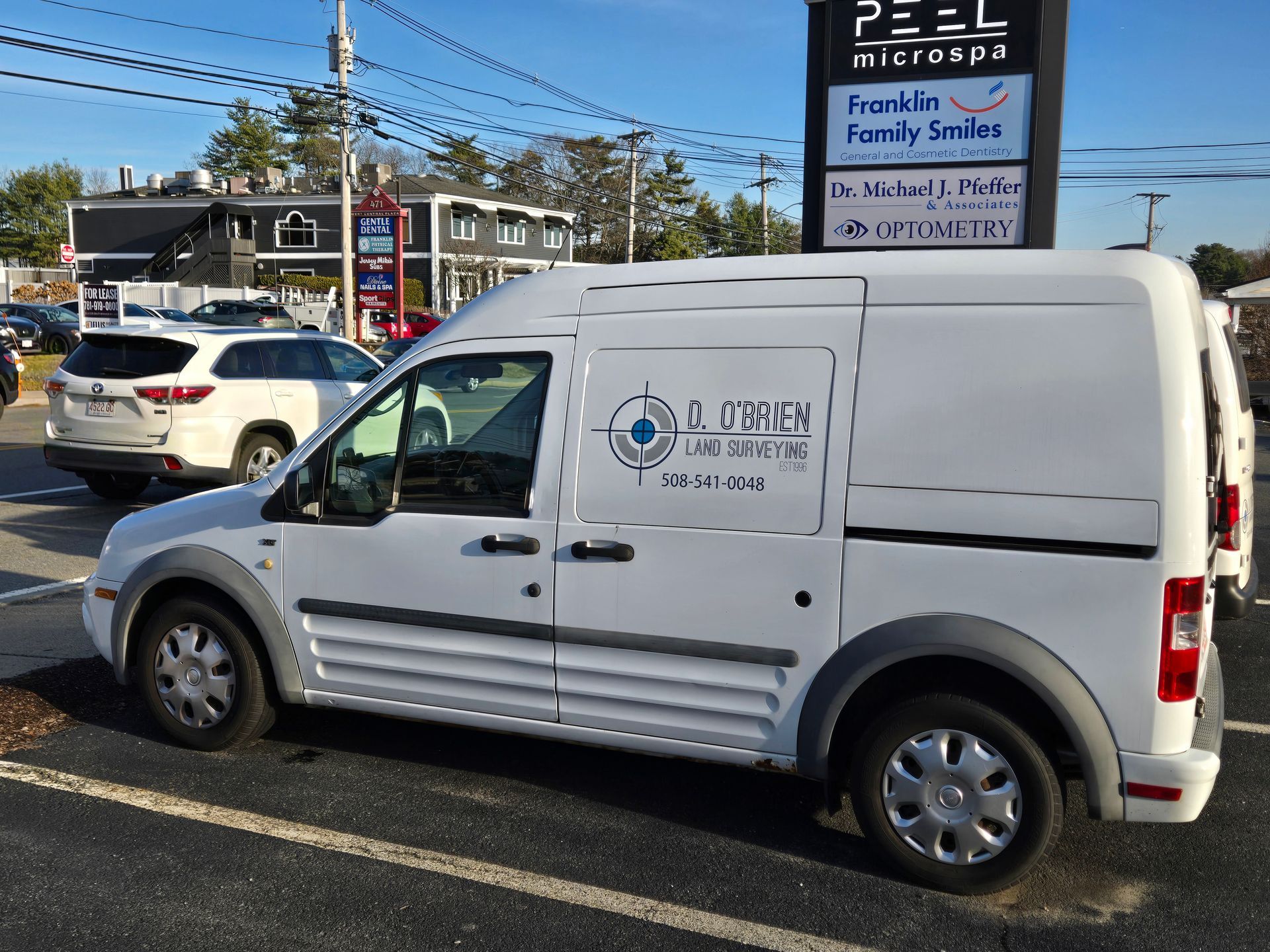 A white van is parked in a parking lot in front of a sign for franklin family services.
