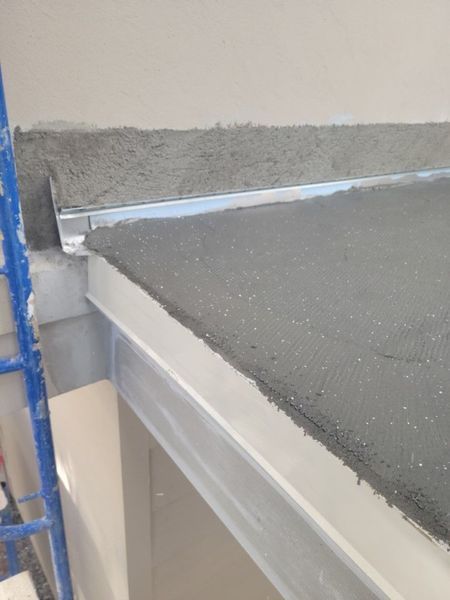 Wet concrete mortar layered over a metal frame and edge flashing during a construction or flooring installation project.