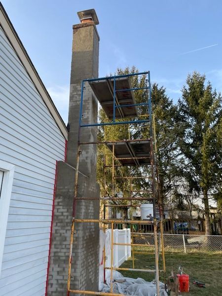 Tall metal scaffolding erected next to a stucco chimney against a house with grey siding under a clear blue sky.