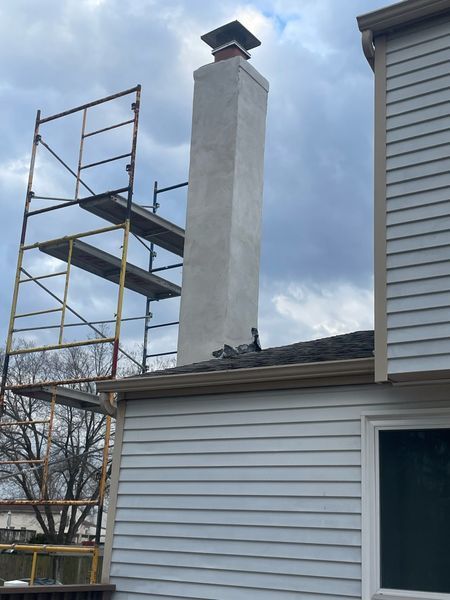 A tall, light-colored stucco chimney stands on a residential roof next to scaffolding.