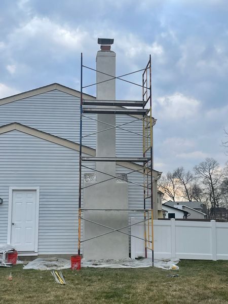 Metal scaffolding set up against a residential chimney being repaired on a bright, cloudy day.