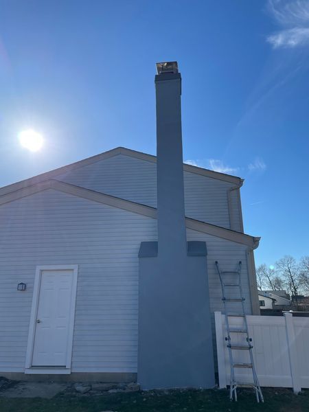 A light blue exterior chimney attached to a light blue house under a bright sunny sky, with a ladder leaning against it.