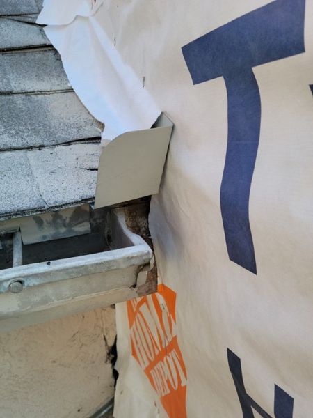 Close-up of a roof edge where a white metal flashing diverter meets house wrap above a gutter.