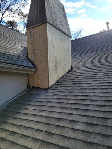 A chimney chase on a roof, with the upper portion finished in dark material and the base currently covered in bare plywood.