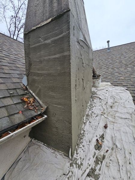 A chimney being resurfaced with textured mortar, shown on a roof with a drop cloth nearby.