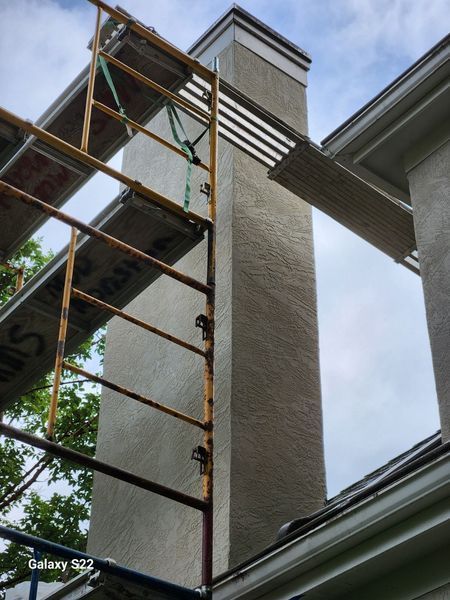 Scaffolding set up against a beige stucco chimney on a house roof.