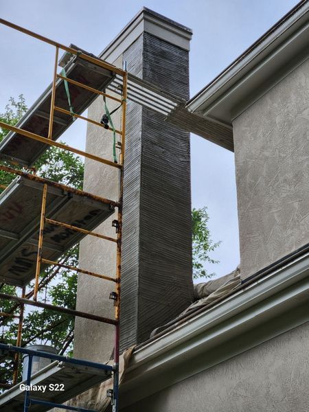 A tall chimney under renovation, with scaffolding in place and a portion of its surface covered in gray adhesive.