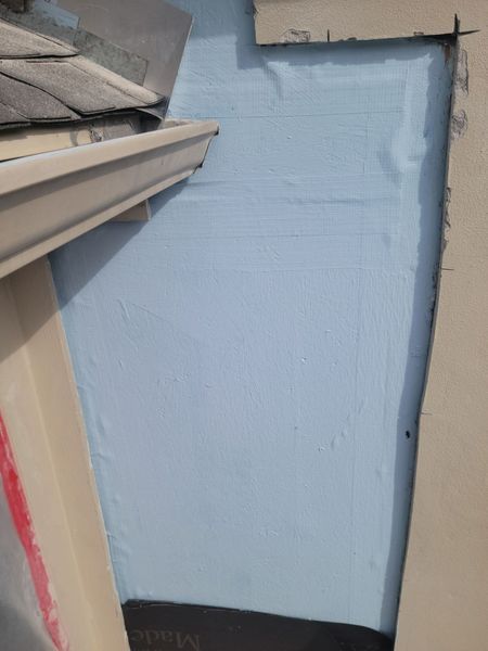 A blue rectangular insulation board installed on a wall next to a roof gutter and exterior siding.