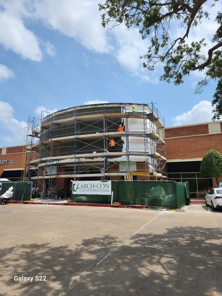 Exterior view of a commercial building renovation with scaffolding covering a curved facade, under a bright blue sky.