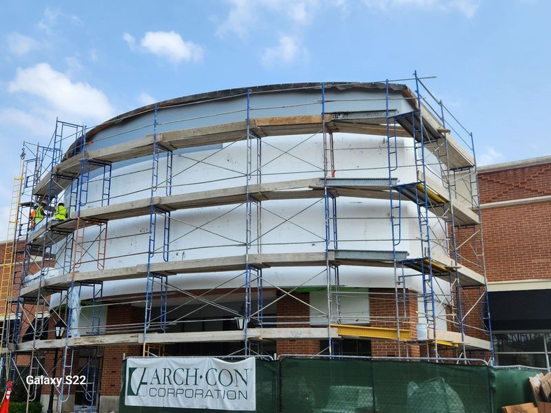 Construction workers on scaffolding around a white, curved building exterior with an Arch-Con Corporation sign below.