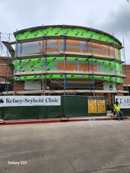 A construction site for a Kelsey-Seybold Clinic featuring a curved building exterior with green scaffolding.