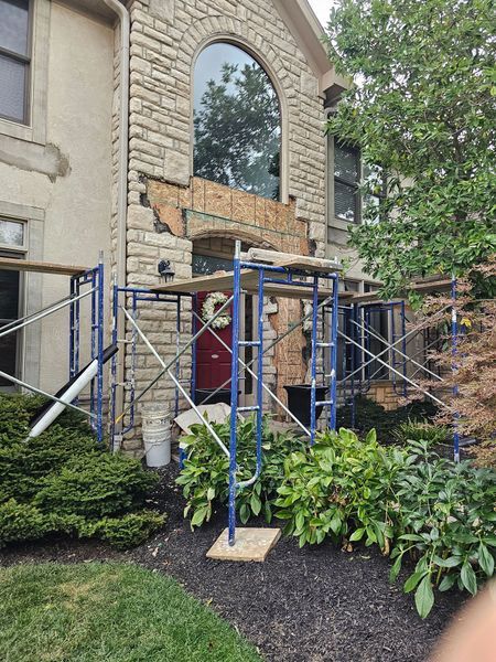 Scaffolding set up in front of a residential house entrance where stone facade siding has been removed above the door.