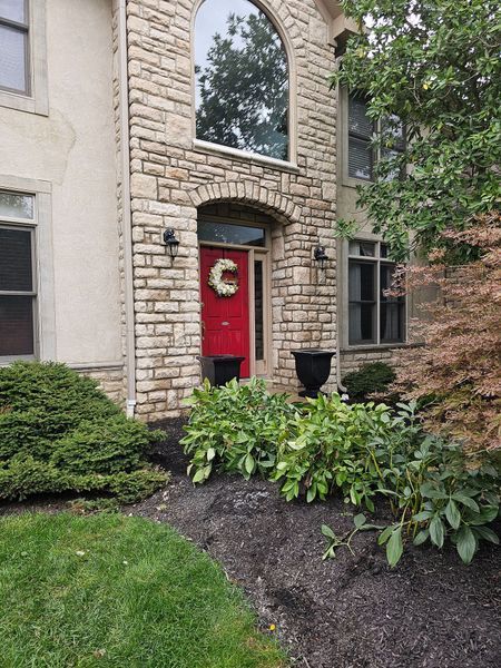Front view of a two-story house with stone facade, a bright red front door, and a landscaped front garden bed.