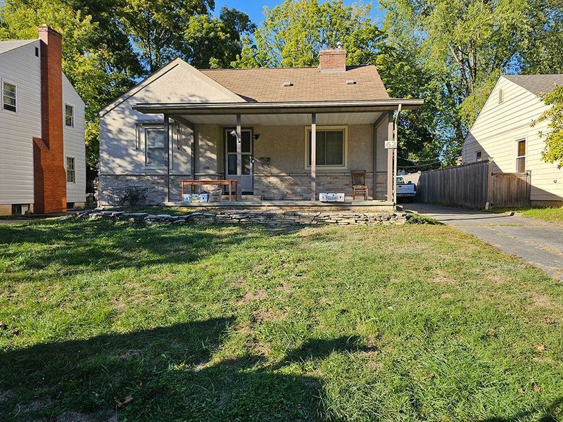 Single-story brick house with a front porch, surrounded by green grass and trees under a clear blue sky.
