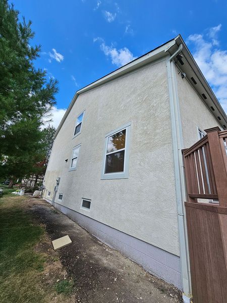 A beige stucco side wall of a house with four windows, a grey foundation, and a partial view of a wooden deck.