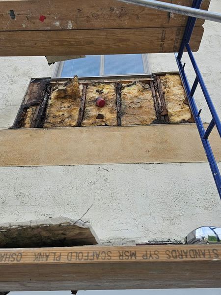 Scaffolding in front of a building facade with a section of exterior wall removed, exposing wood studs and insulation.
