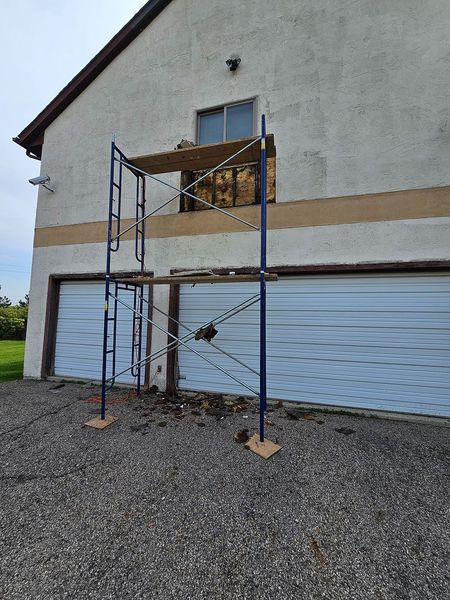 Blue scaffolding stands in front of a house with a hole in the exterior wall below a window.