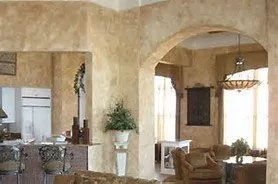 A home interior with textured beige walls, arched doorways, a kitchen area on the left, and a living space on the right.