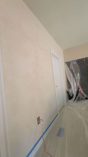 A freshly plastered interior wall painted a light cream color, with blue painter's tape along the bottom and plastic cover.
