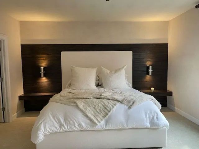 A bedroom features a white upholstered bed centered against a horizontal dark wood accent wall with integrated shelf lights.