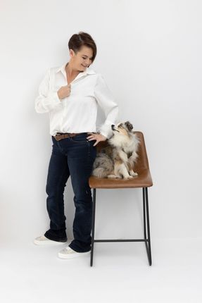 A woman is standing next to a dog sitting on a chair.