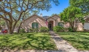 A brick house with a lush green lawn and trees in front of it.