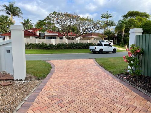 Brick driveway leads to street; white truck drives past houses on a sunny day.
