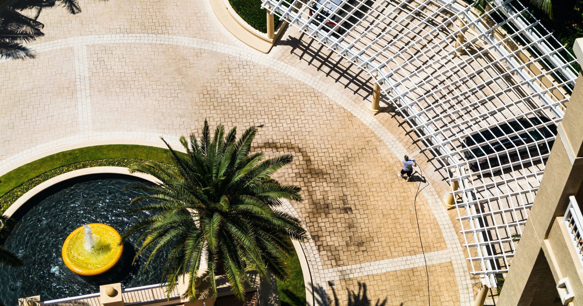 Overhead view of a circular driveway with a fountain, palm tree, and a person walking under a pergola.