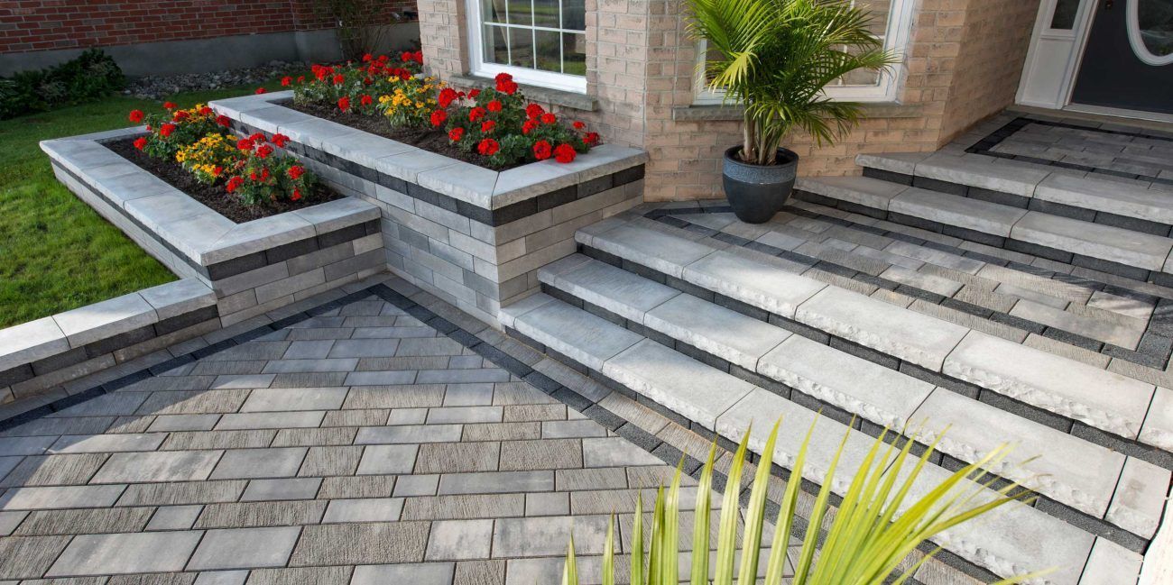 Stone steps and flower beds leading to a home with a palm tree in a pot.