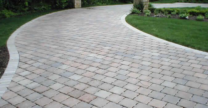 Curved brick paver driveway with green grass and foliage bordering it.
