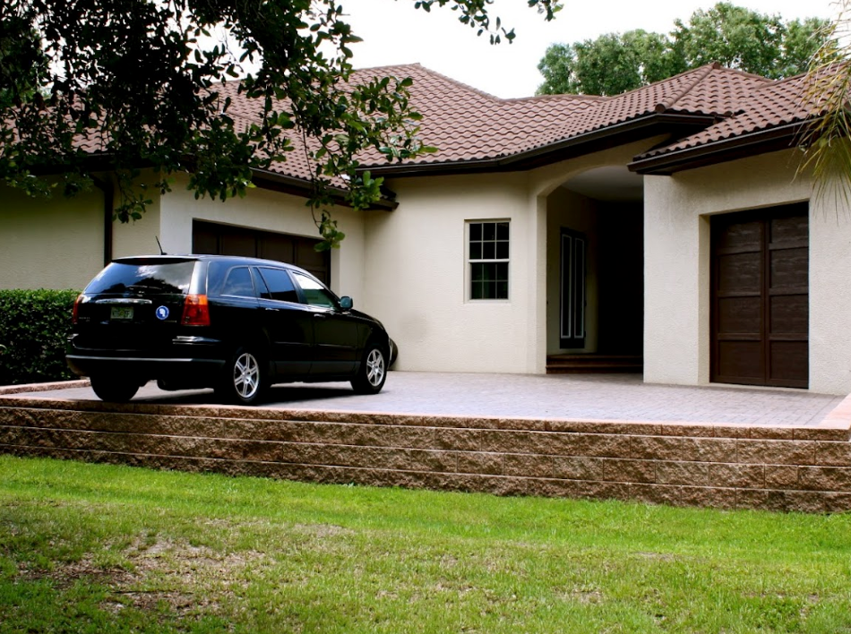 Black SUV parked in front of a tan house with brown garage doors and a red-tiled roof.