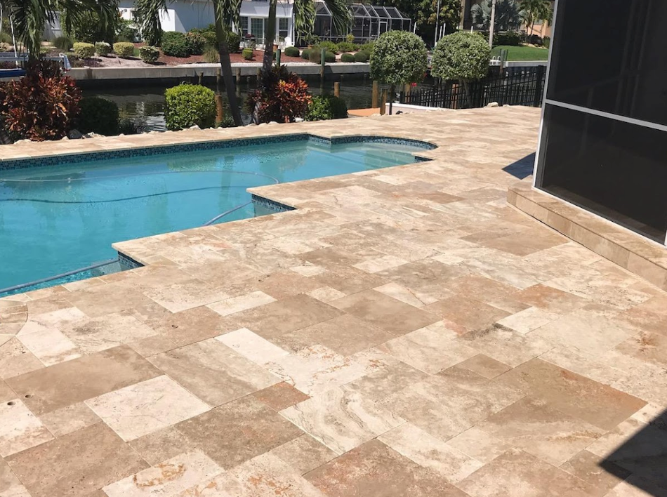 Swimming pool with beige stone patio, overlooking a canal. Lush greenery surrounds the water.