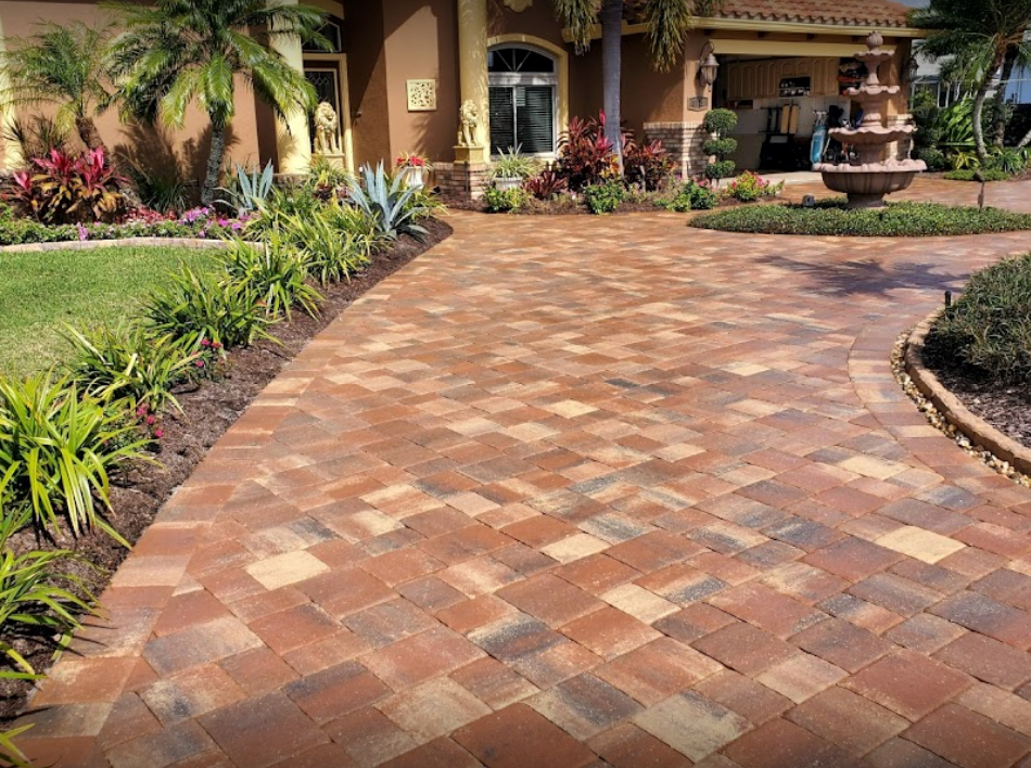 Brick paved driveway leading to a house with landscaping and a fountain.